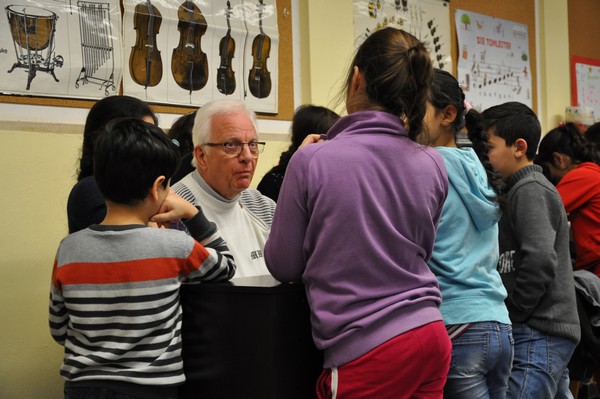Ehrenamtlicher Günter Brummundt spielt „Frère Jacque“ am Klavier – umringt von Grundschulkindern, die das Lied im Takt mit ihren Instrumenten begleiten